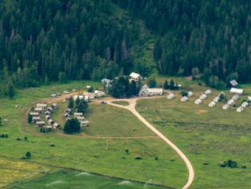 A contemporary color aerial photograph of Camp Davis. A road runs to the center through a field of green. Rows of cabins populate one side of the photograph. The other side shows buildings built along a curving path.